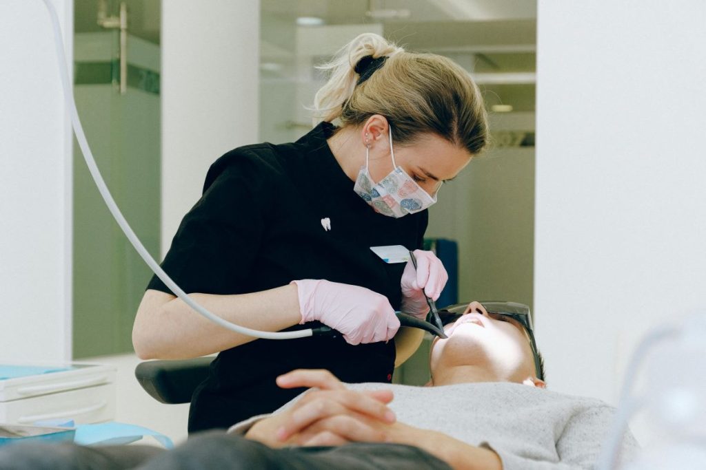 Dentist holding instruments while performing teeth cleaning on a young patient