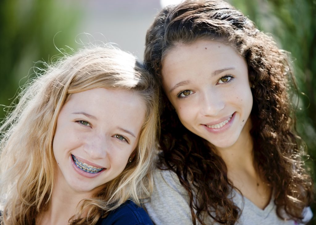 Two young girls smiling with one wearing metal and plastic braces for orthodontics treatment at Burlington Family Dentists. Braces in Burlington