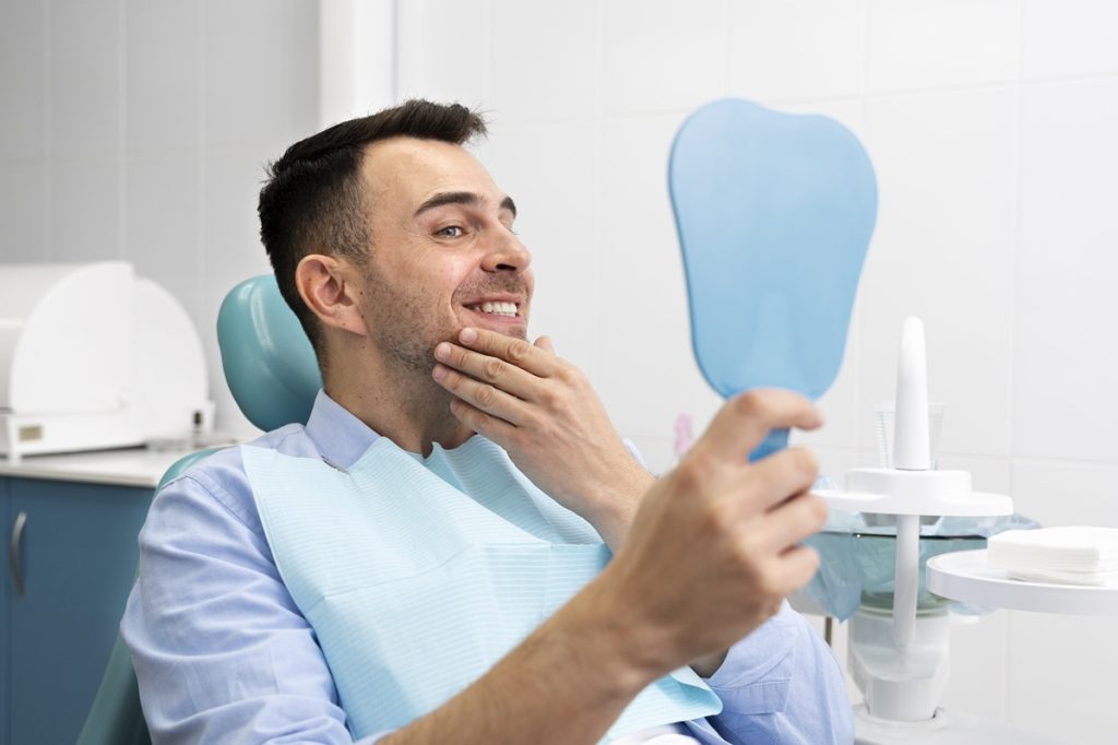 Young man smiling and checking his dental implant results in a clinic mirror.