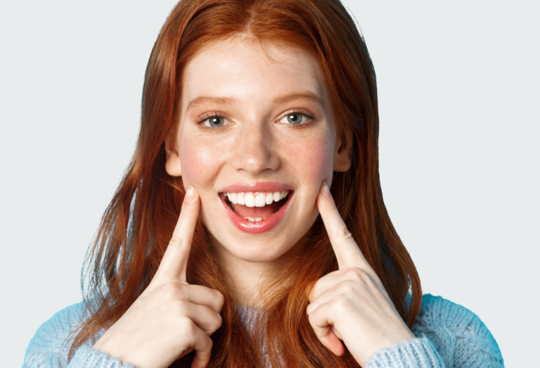 Young woman pointing at her smile after full mouth rehabilitation.