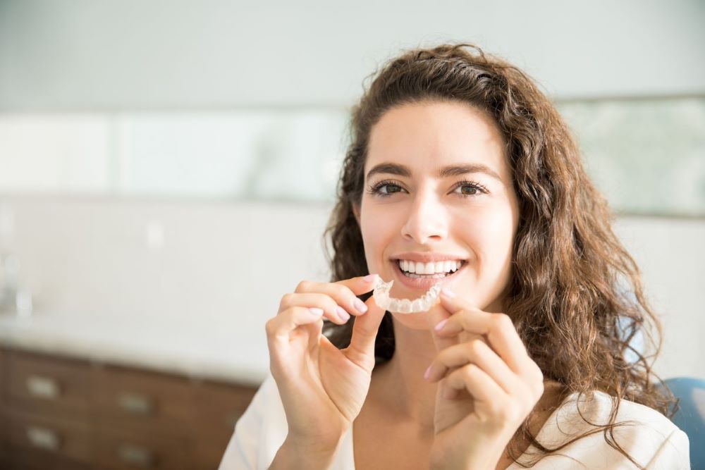 Smiling young woman holding clear aligners near her mouth.