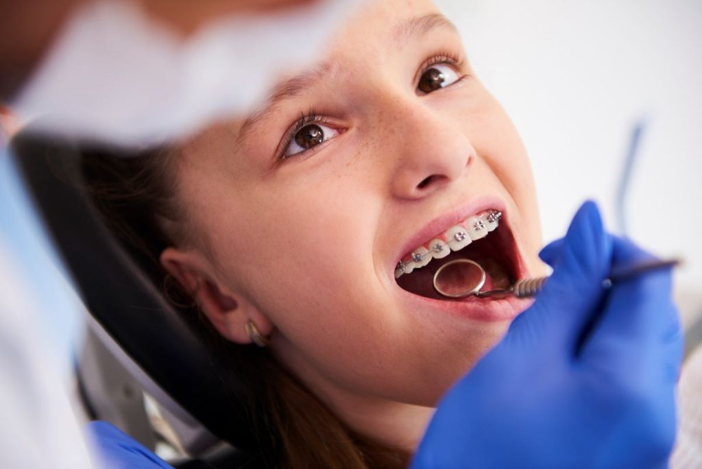 Dentist examining a young girl’s teeth with orthodontic braces