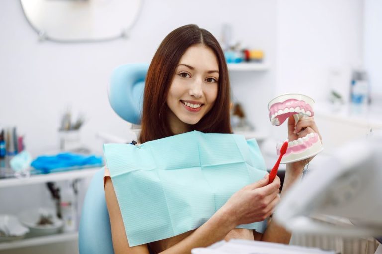 Smiling young woman holding a dental model and toothbrush.