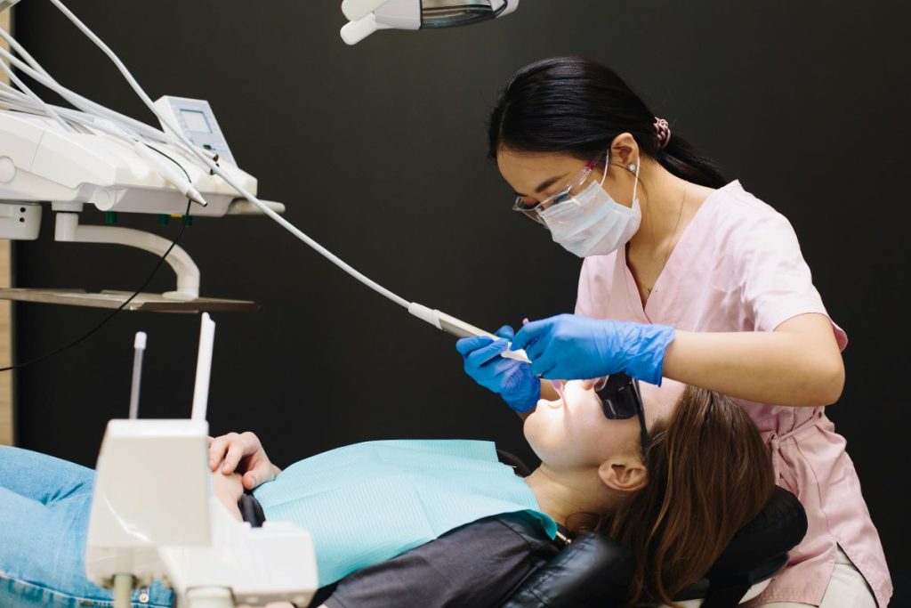 Dentist using sterilized instruments to clean a young patient’s teeth