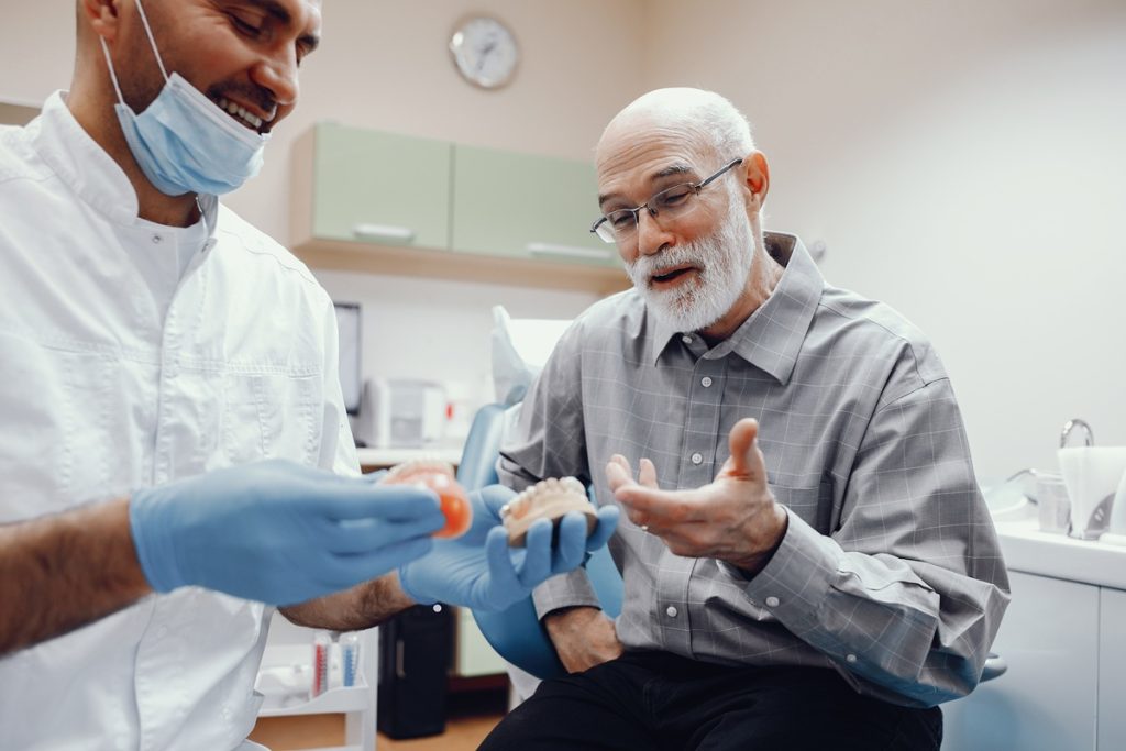 Senior man consulting with dentist about dentures and dental implant samples.